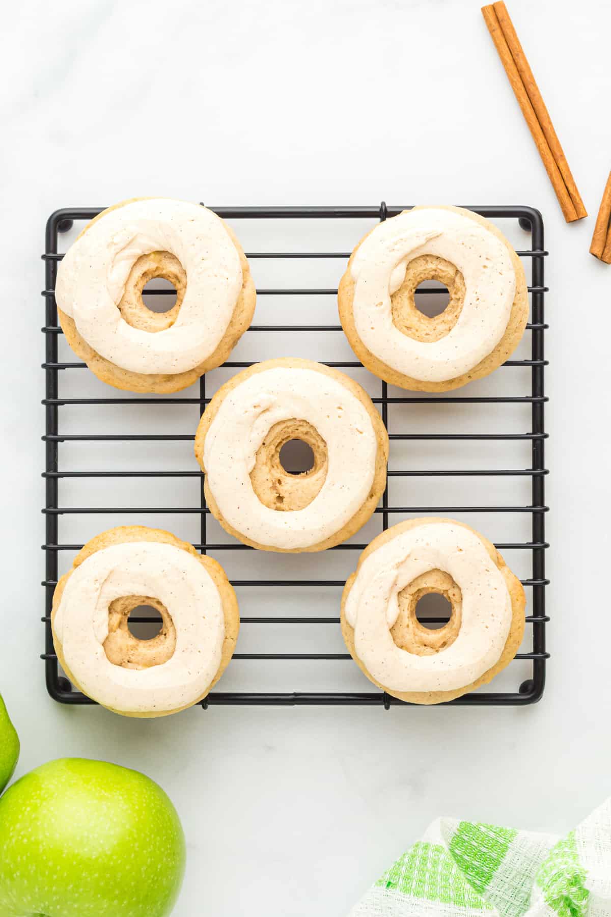 five frosted apple donuts arranged on a cooling rack
