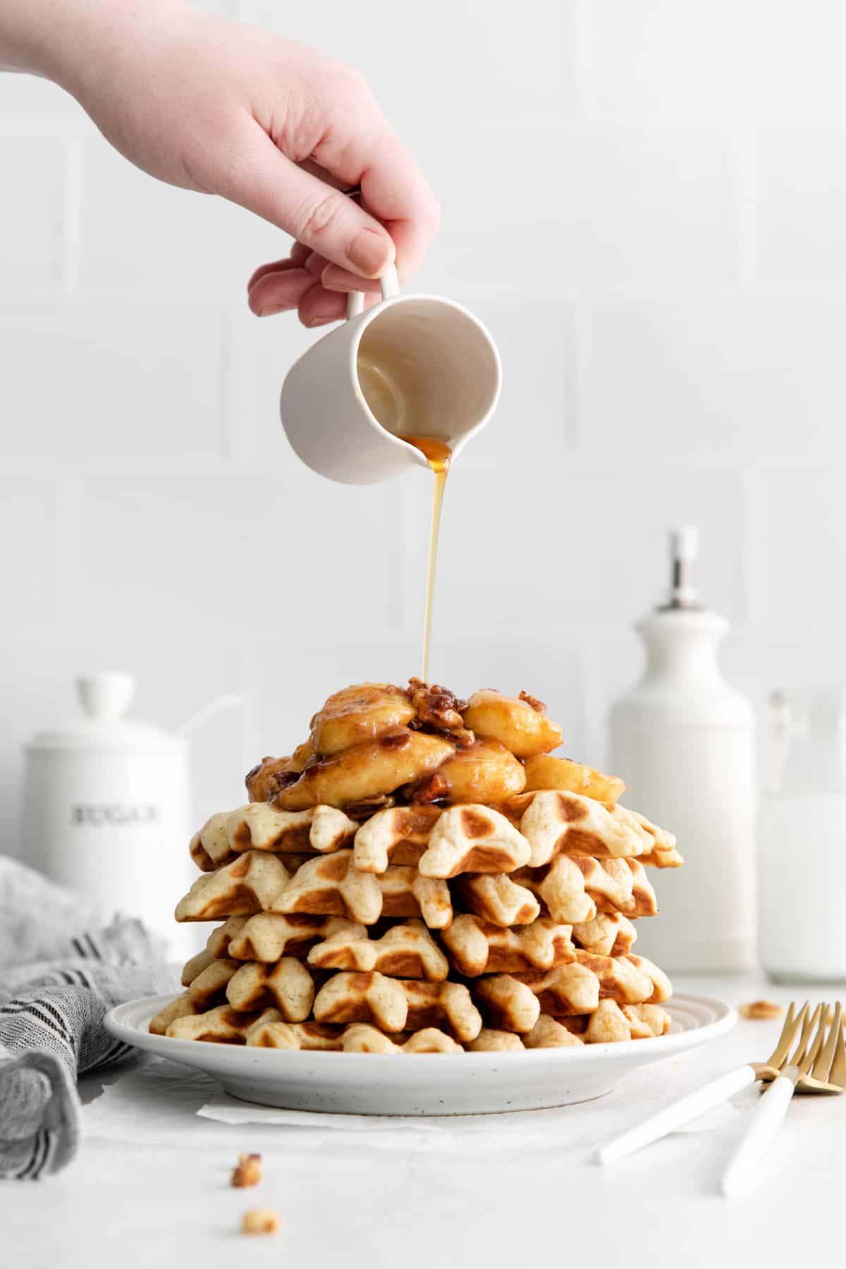 pouring syrup over a stack of waffles