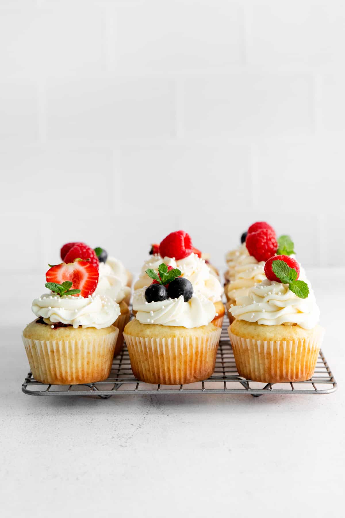 berry filled cupcakes, topped with frosting and fresh berries, lined up on a cooling rack