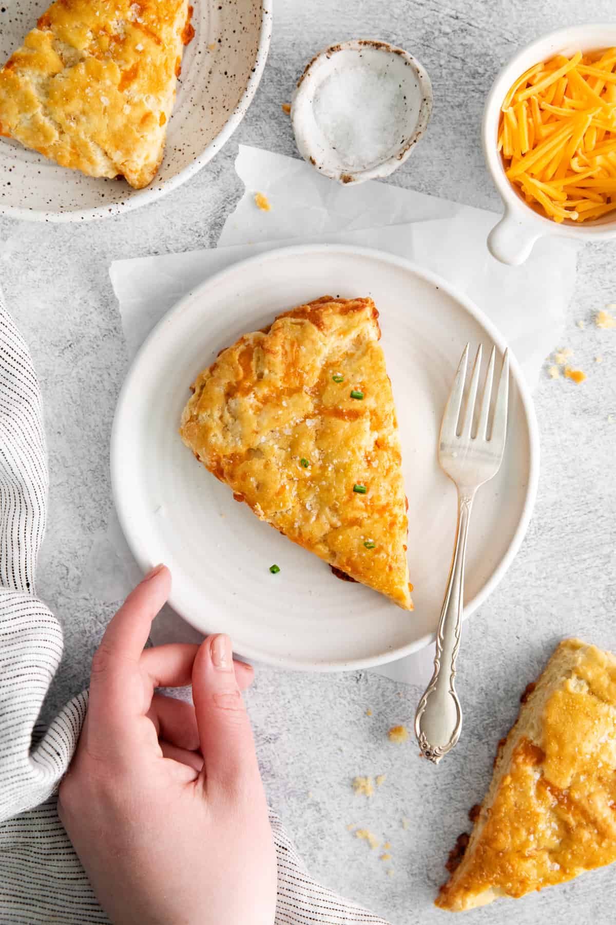 hand reaching for a plate with a cheese scone on it