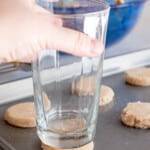 using a glass to push down and flatten the cookie dough