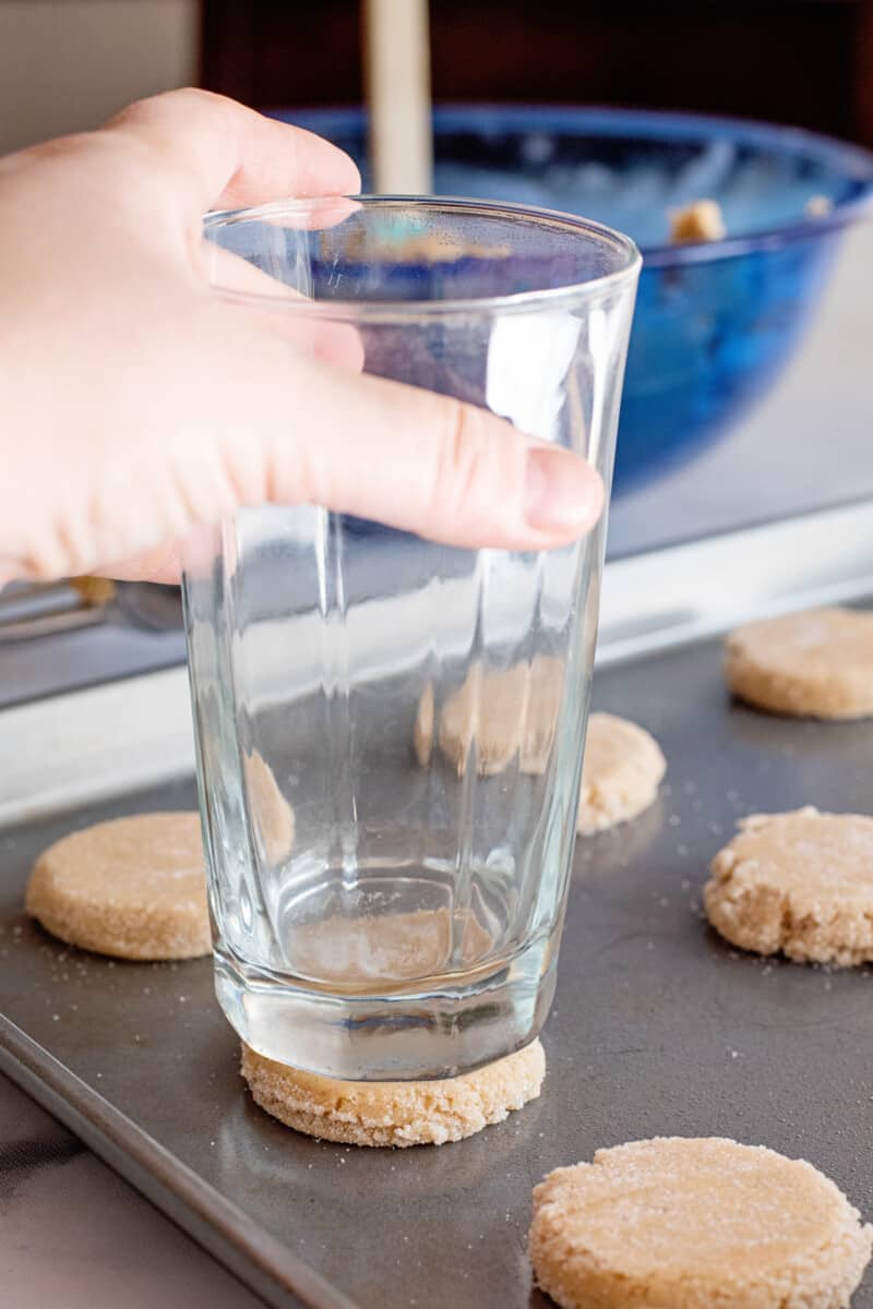 using a glass to push down and flatten the cookie dough