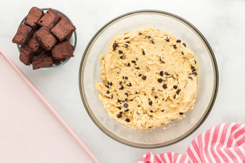 a bowl of chocolate chip cookie dough next to a smaller bowl of brownies cut into cubes
