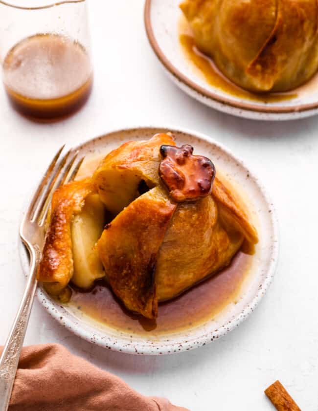 a cut apple dumpling on a white plate with a fork.