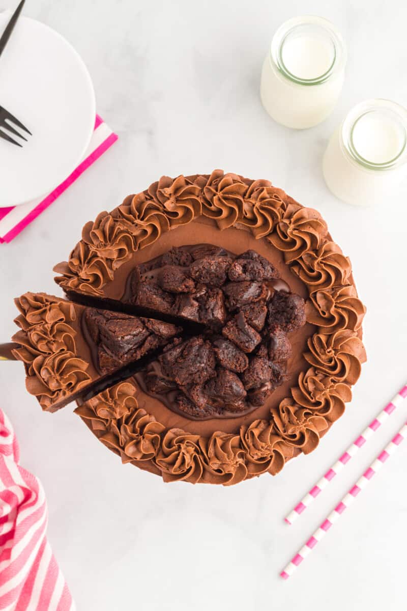 overhead view of a slice of brownie cake being cut form a cake on a cake stand.