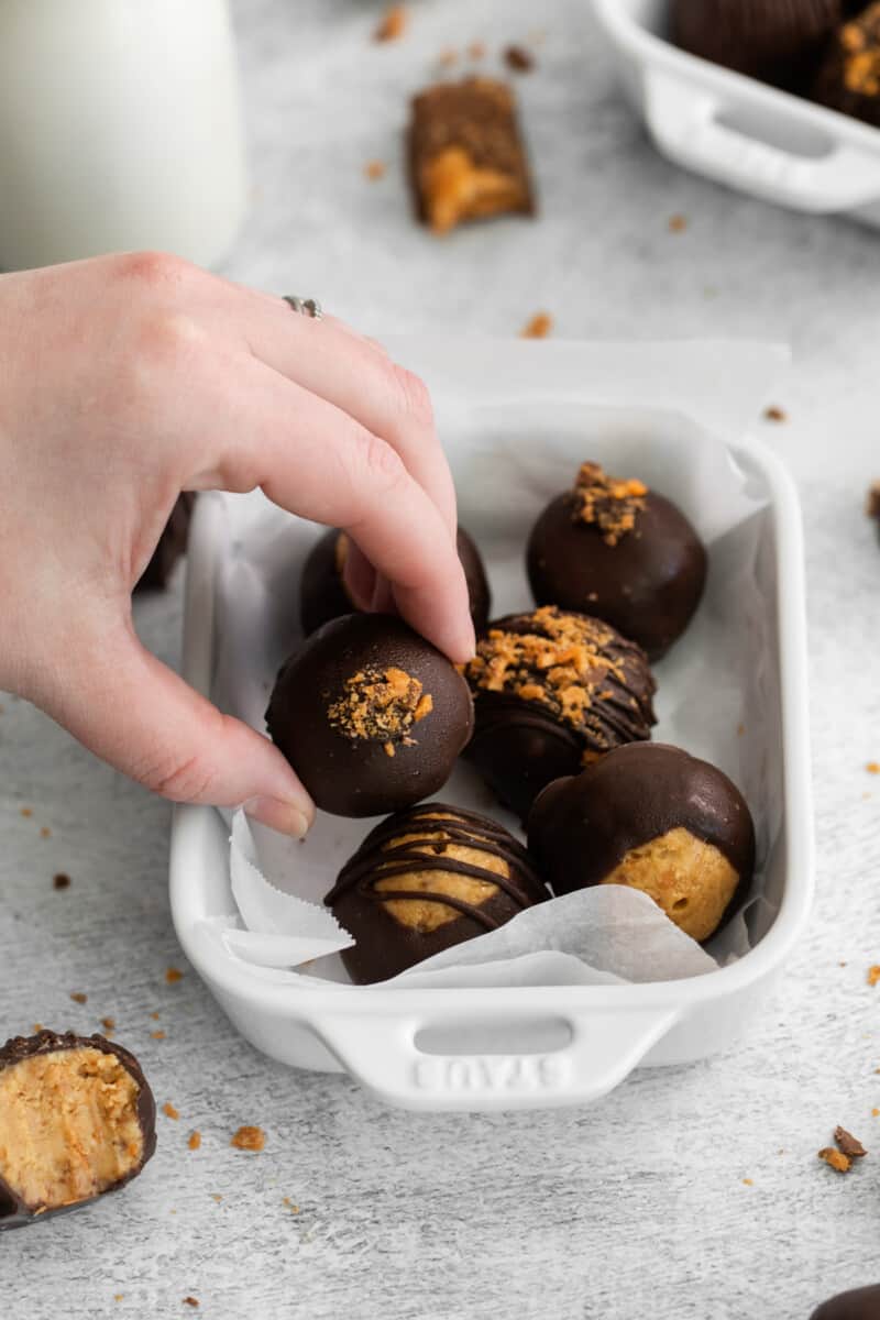 a hand grabbing 1 of 6 butterfinger balls from a white serving dish.