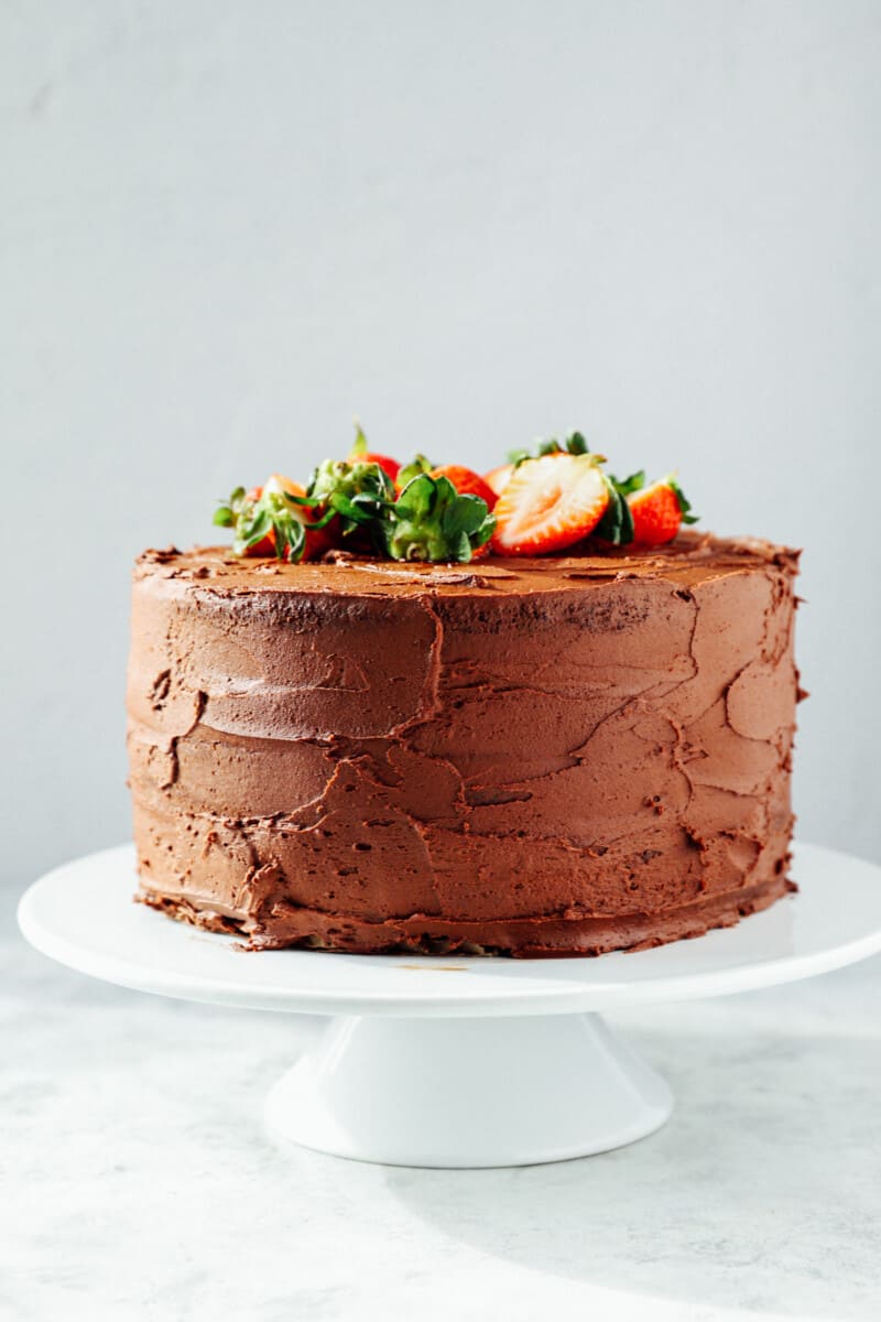 chocolate strawberry cake with strawberries on top on a white cake stand.