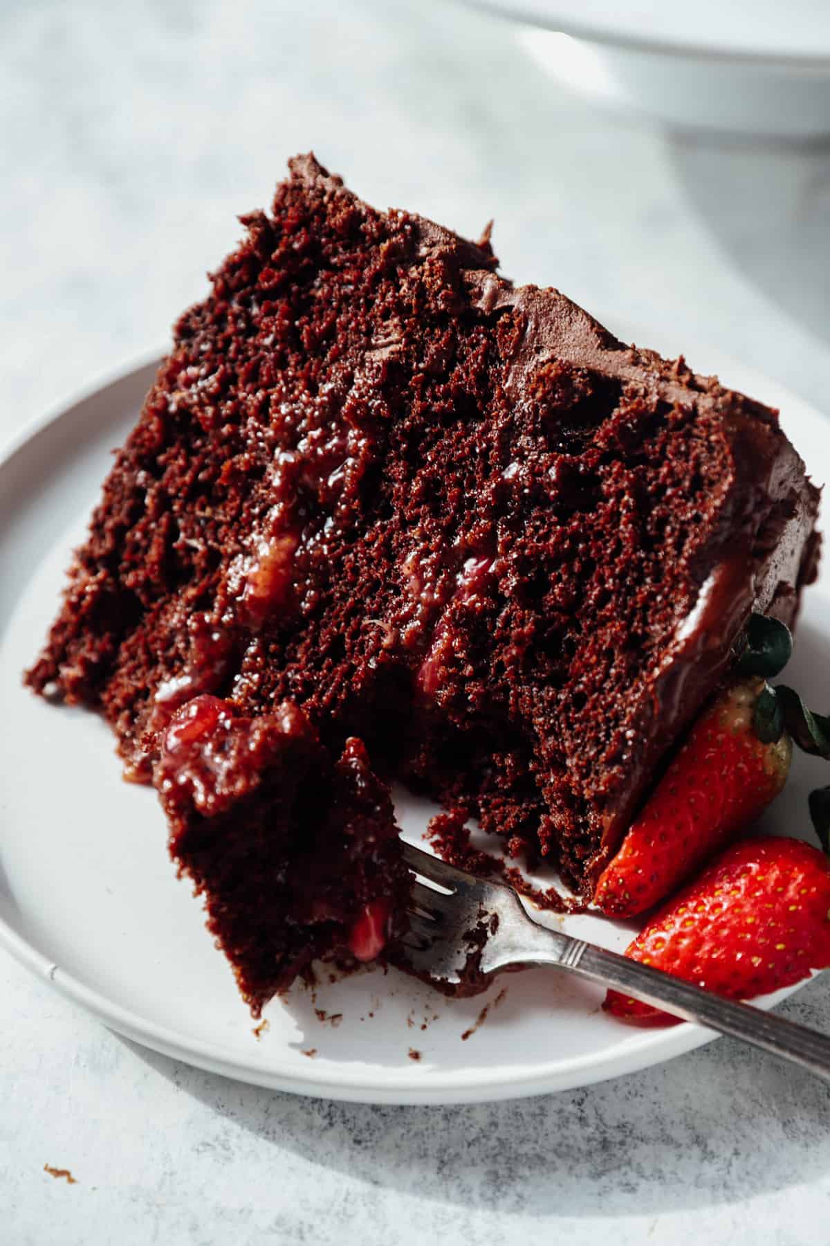 a forkful of chocolate strawberry cake on a white plate with a slice of cake.