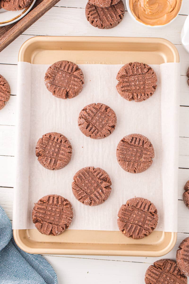 overhead view of 8 chocolate peanut butter cookies on a lined baking sheet.