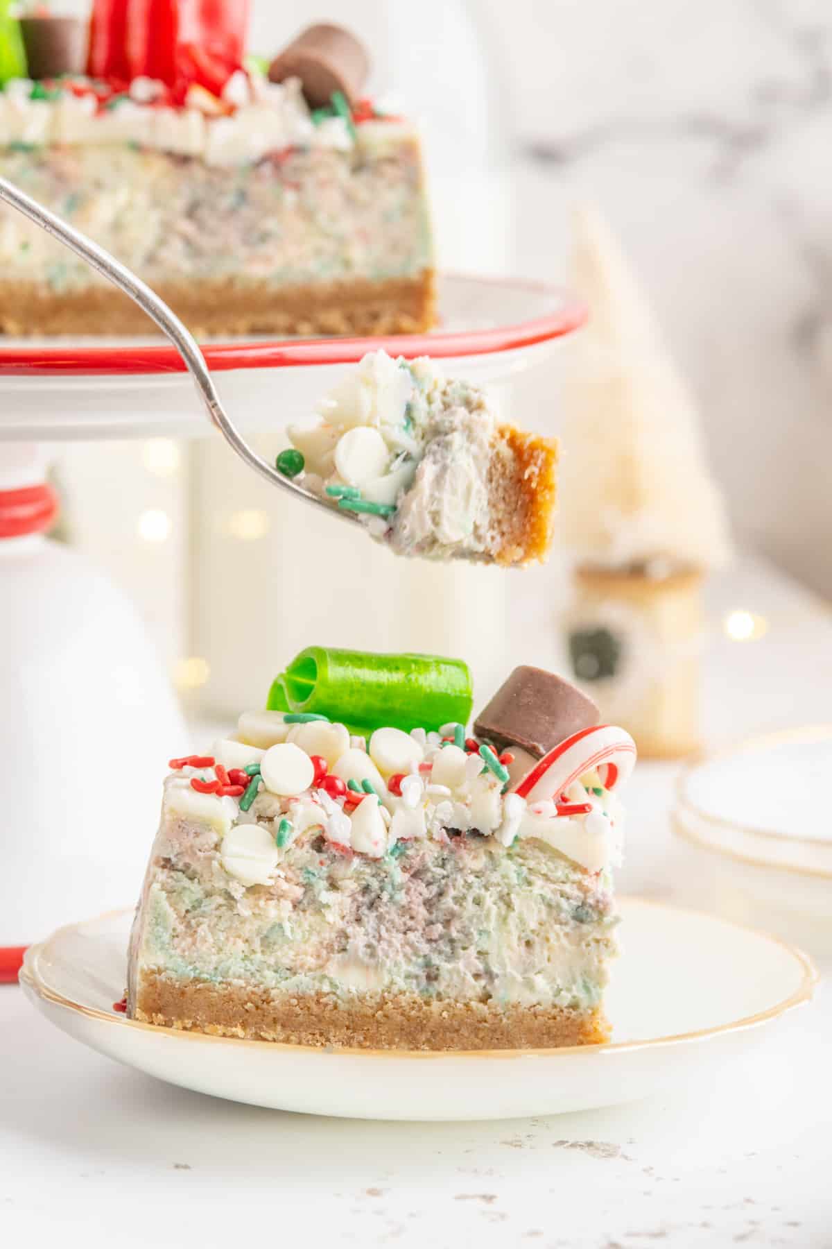a forkful of christmas cheesecake suspended above a slice of christmas cheesecake on a white plate.