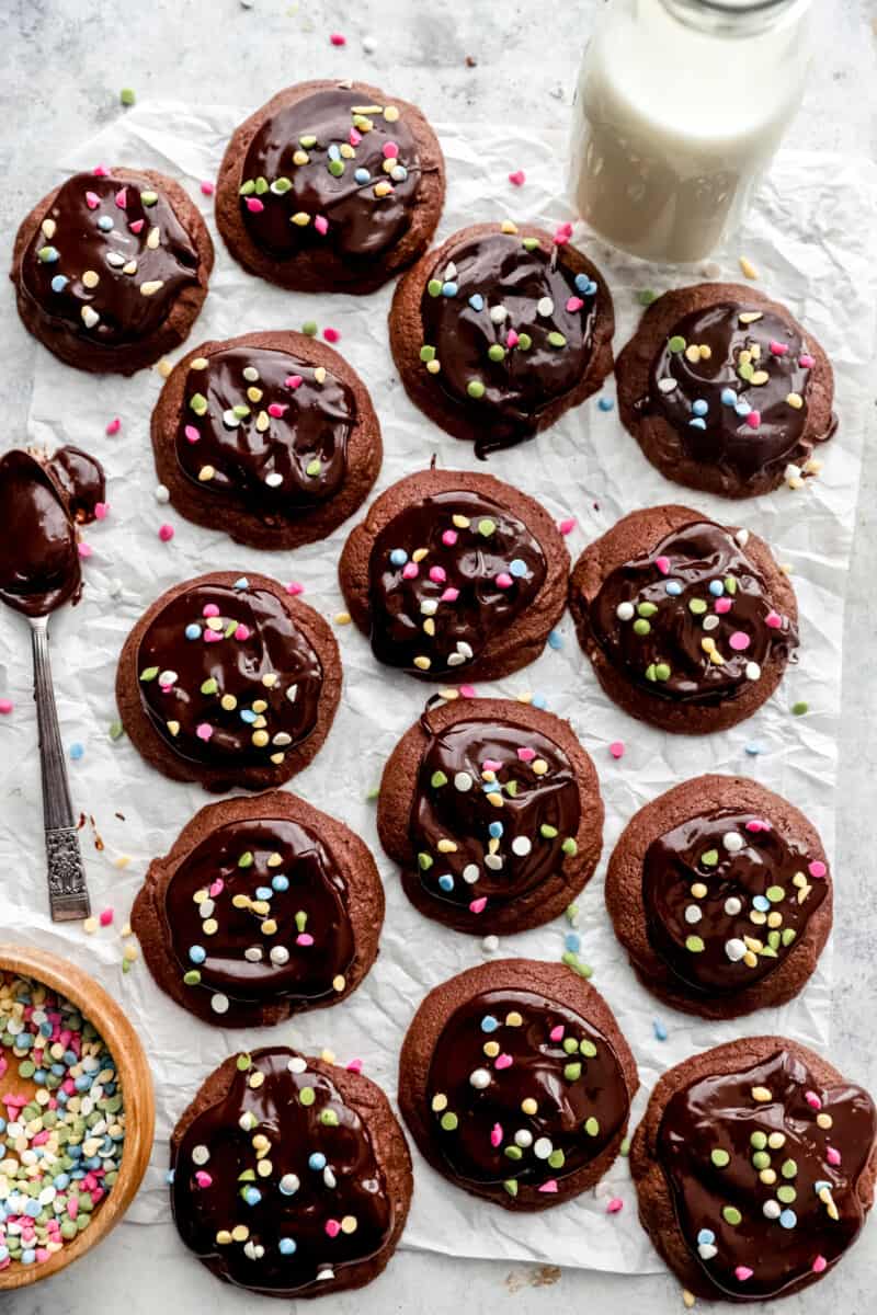 14 cosmic brownie cookies on parchment paper with a ganache coated spoon.