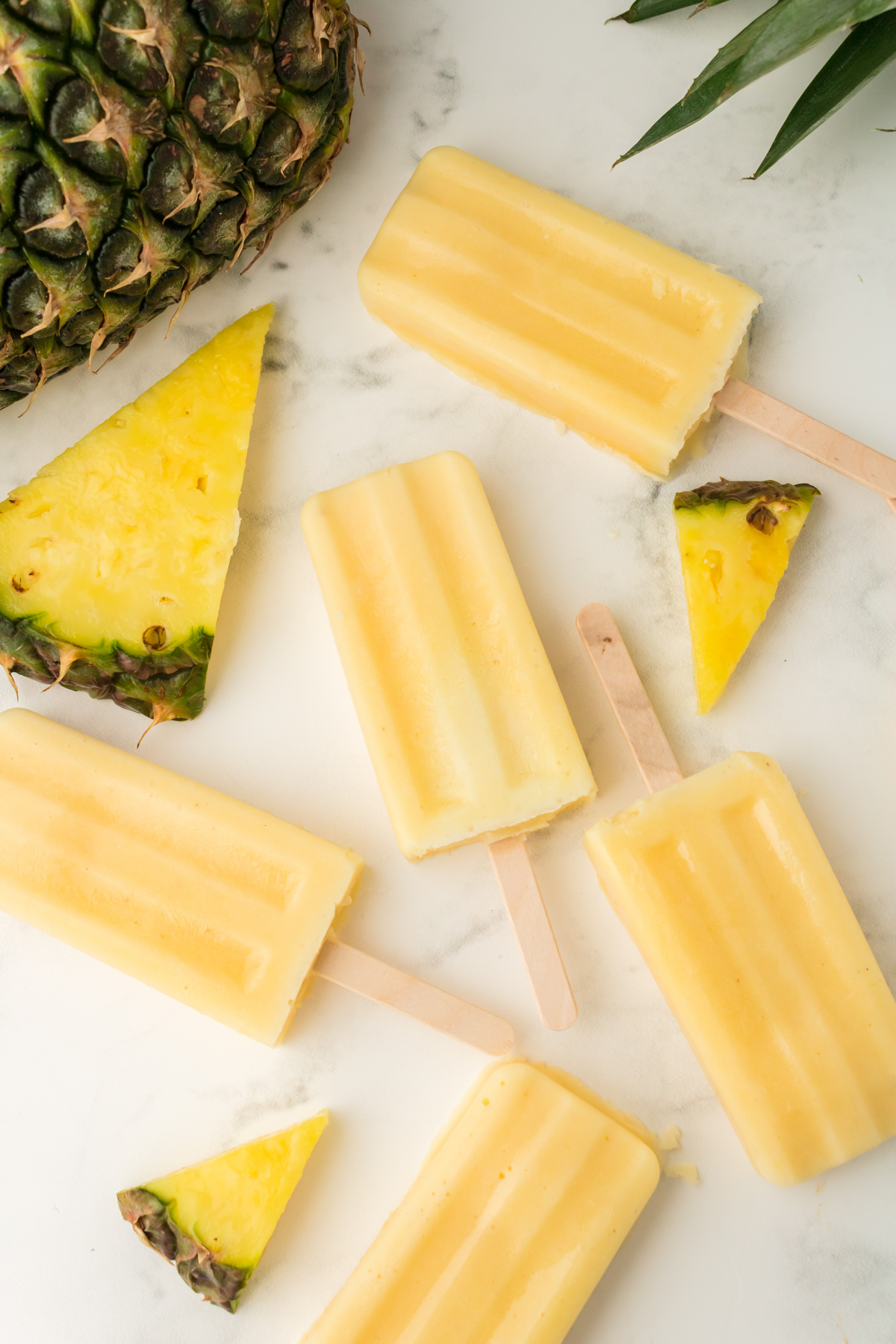 ice cream dole whip popsicles laid on a countertop with pineapple slices