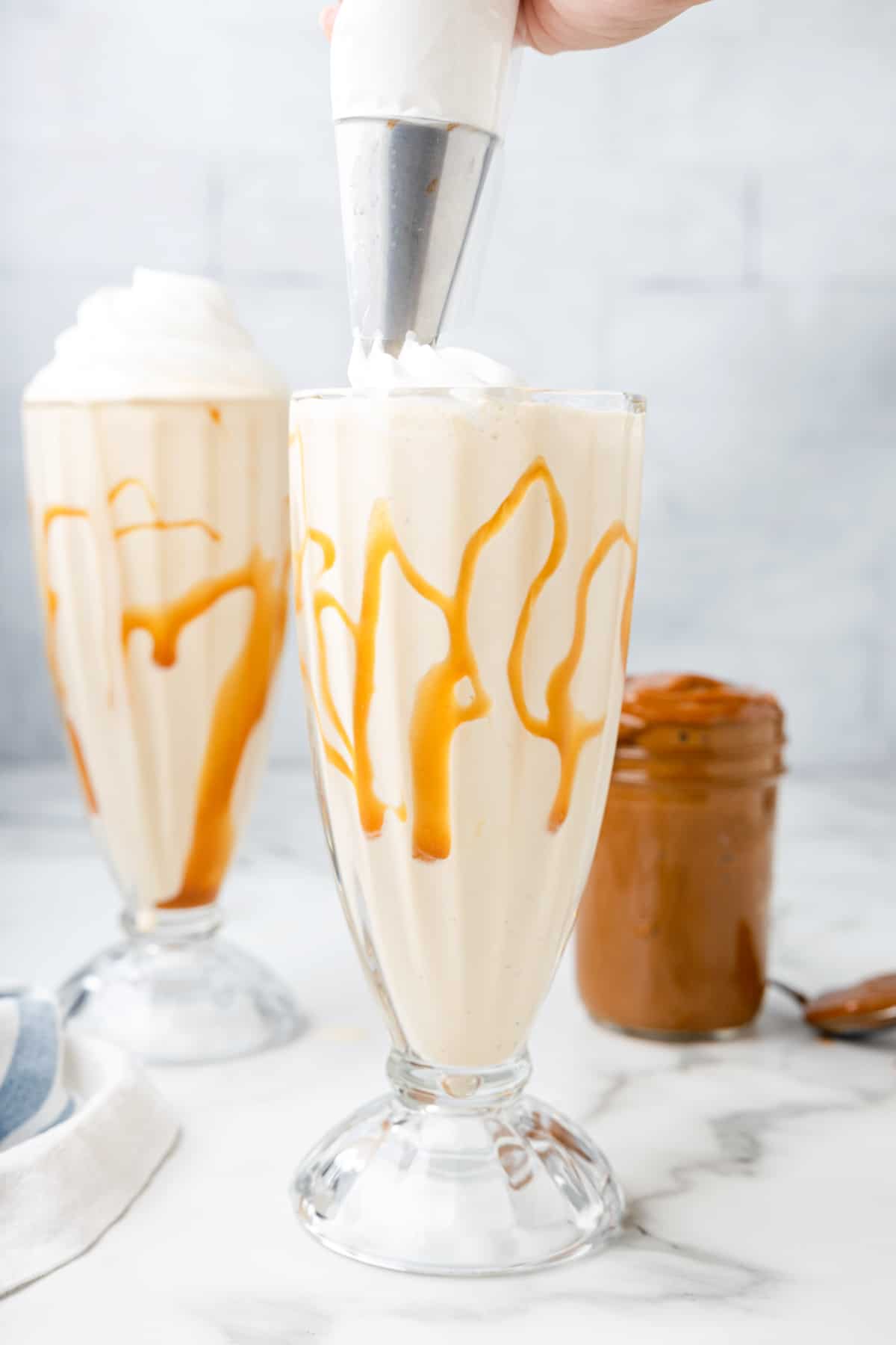 piping whipped cream on top of a dulce de leche milkshake