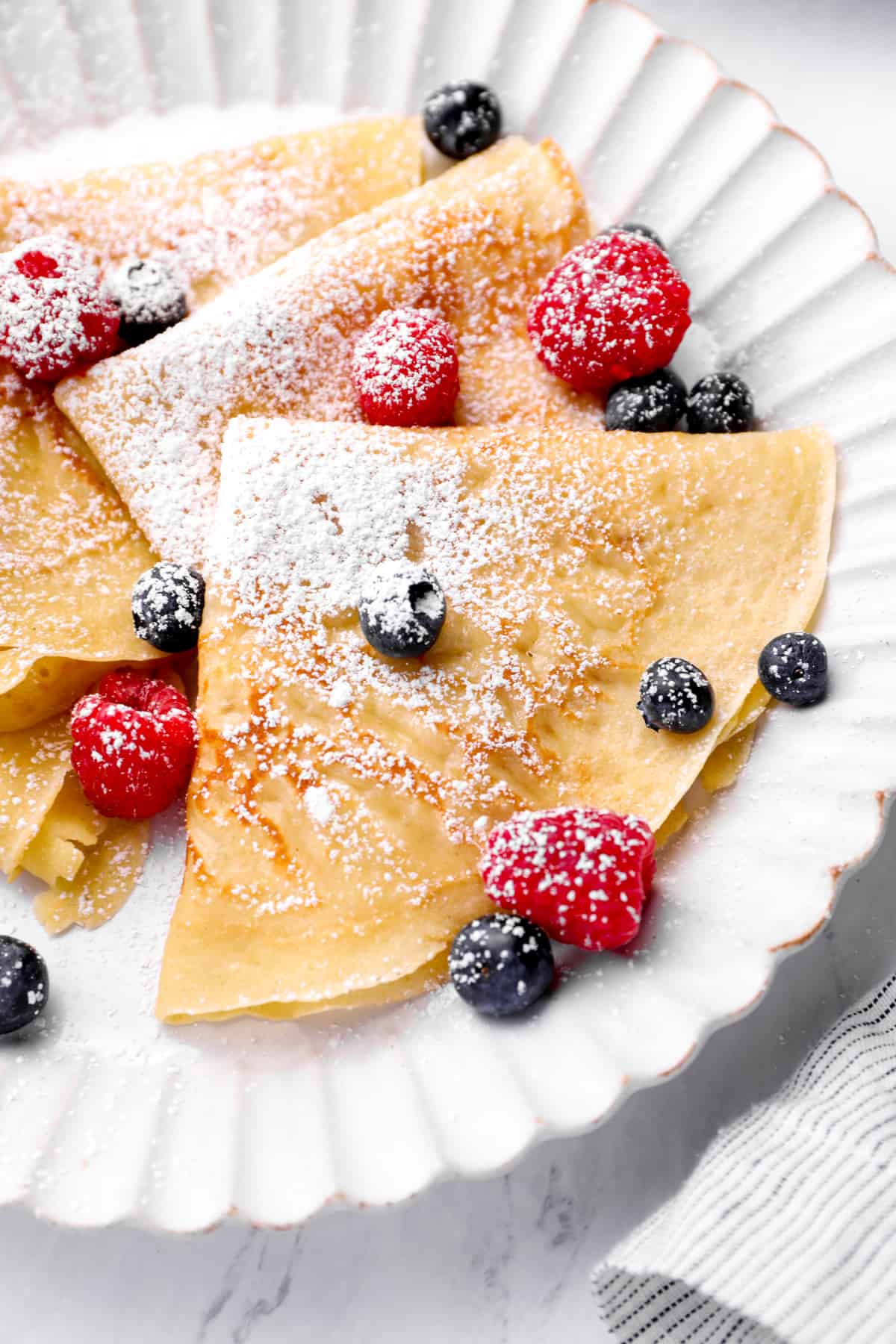 a plate of homemade crepes with berries and powdered sugar