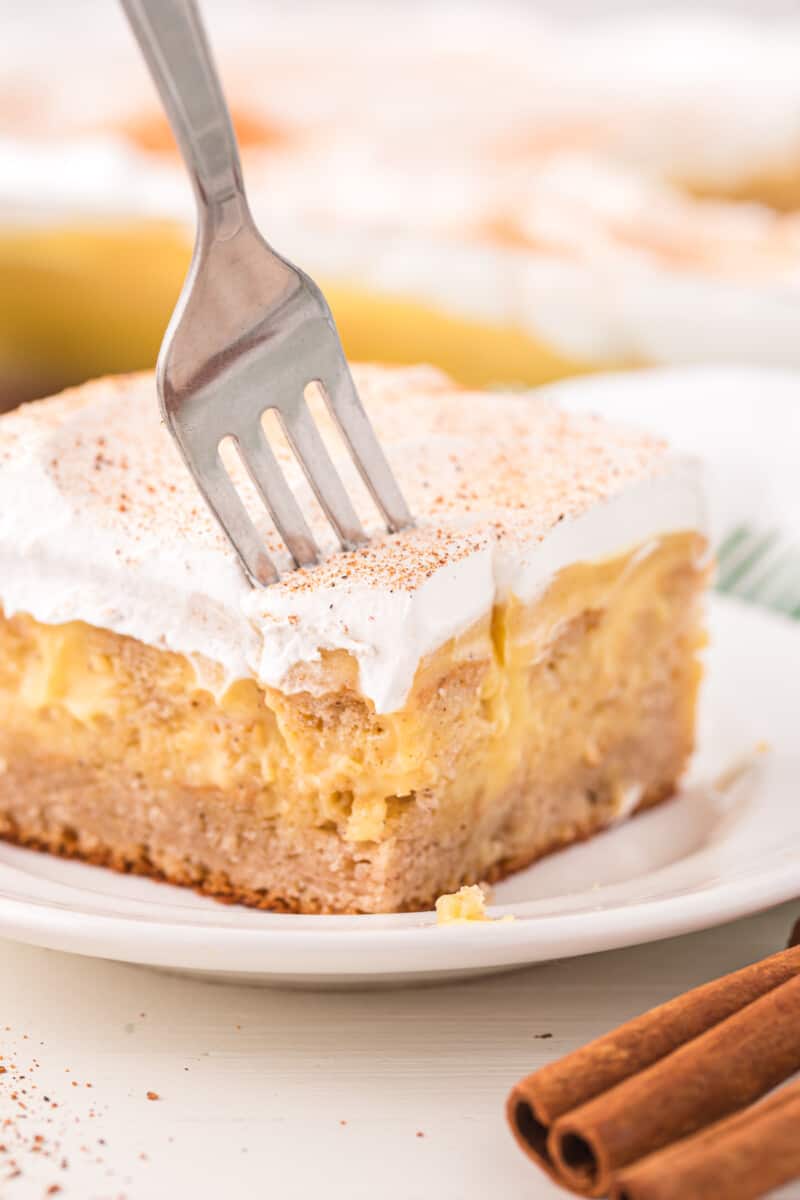 a fork stabbing a slice of eggnog poke cake on a white plate.