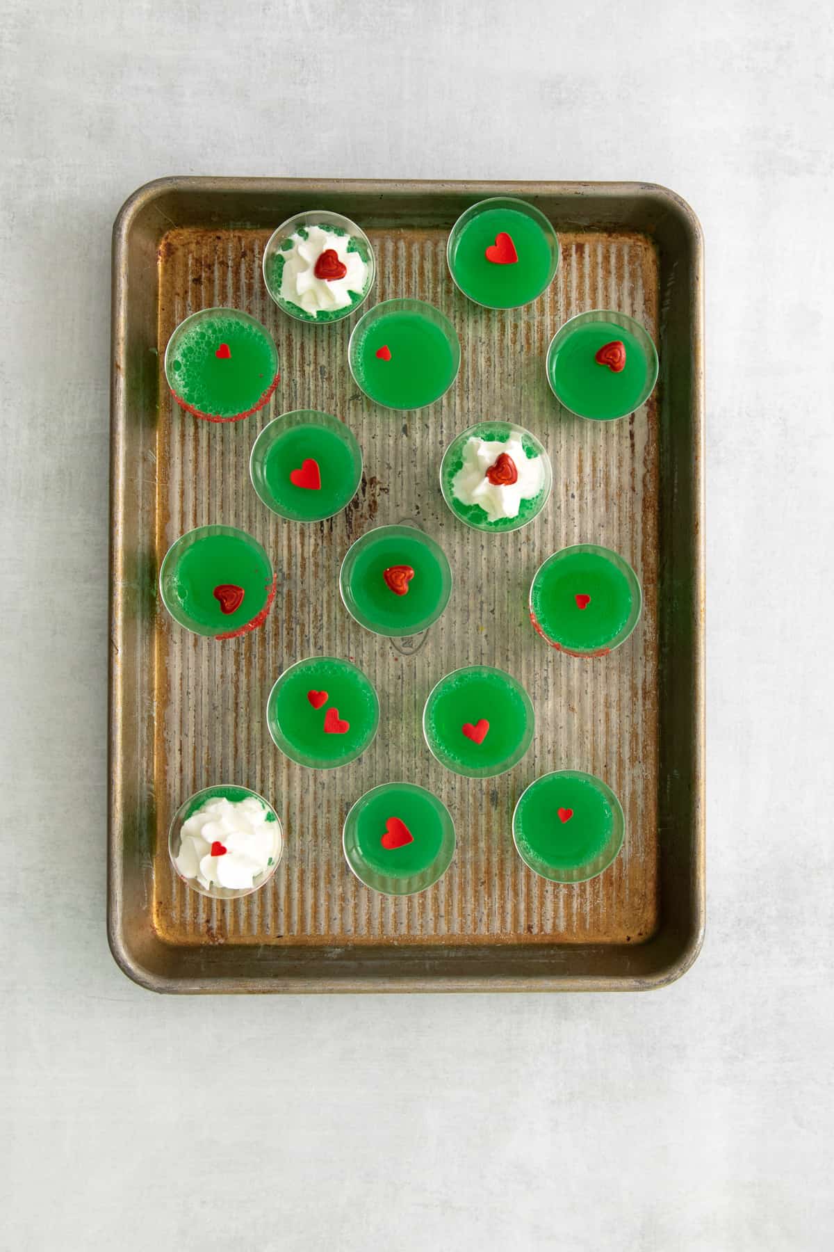 overhead view of 15 grinch jello shots on a rimmed baking sheet.