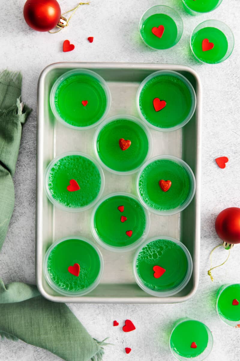 overhead view of 8 grinch jello shots on a rimmed baking sheet.
