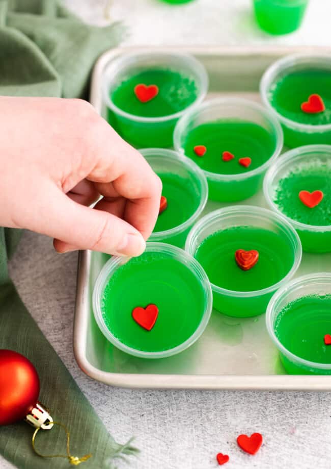 a hand grabbing 1 of 8 grinch jello shots from a rimmed baking sheet.