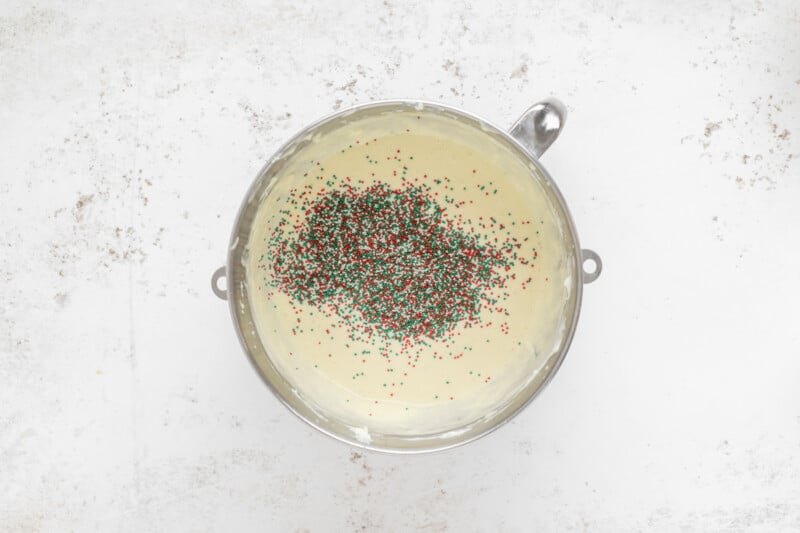 sprinkles added to christmas cheesecake batter in a stainless mixing bowl.