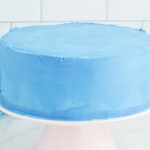 side view of a frosted airplane cake on a white cake stand.