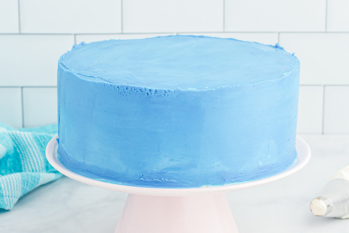 side view of a frosted airplane cake on a white cake stand.