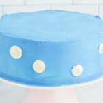 side view of clouds dotted on a frosted airplane cake on a white cake stand.