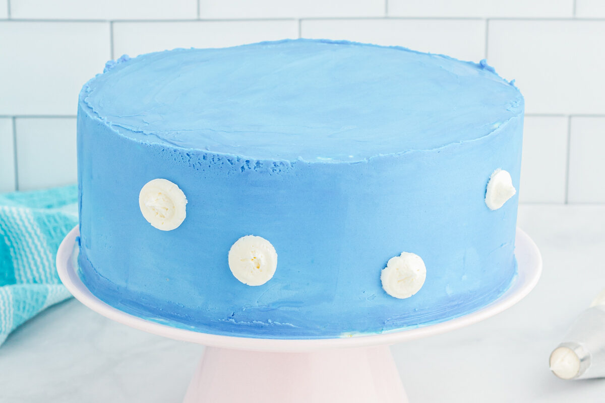 side view of clouds dotted on a frosted airplane cake on a white cake stand.