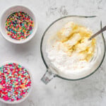 a bowl of powdered sugar, a bowl of flour, and a bowl of sprinkles.