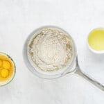 a bowl of flour, eggs and oil on a marble table.