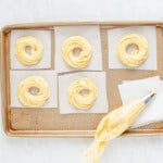 piping batter into cruller shapes on a baking tray