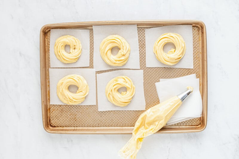 piping batter into cruller shapes on a baking tray