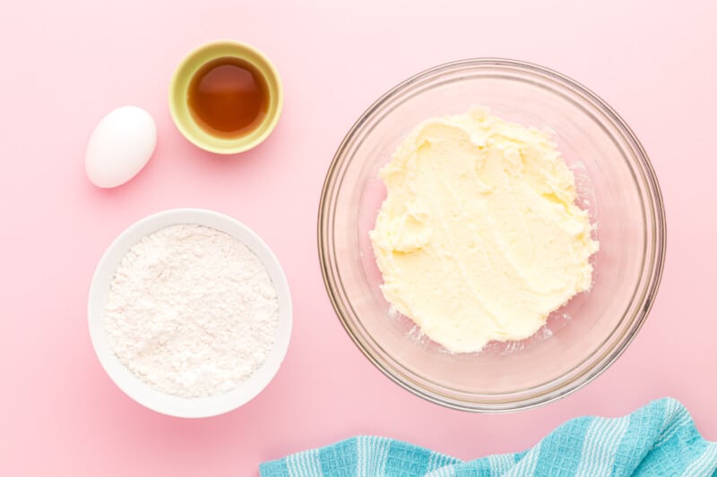 a bowl of butter, eggs and sugar on a pink background.