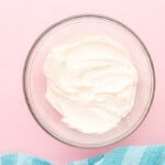whipped cream in a glass bowl on a pink background.