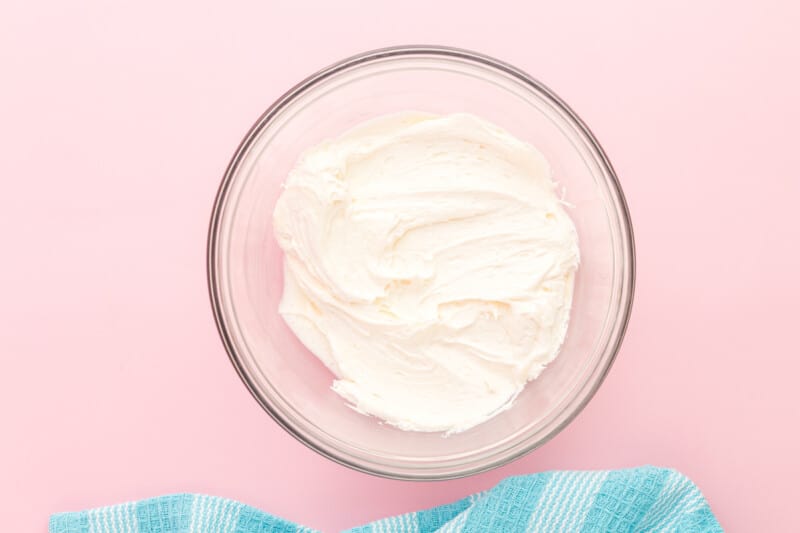 whipped cream in a glass bowl on a pink background.