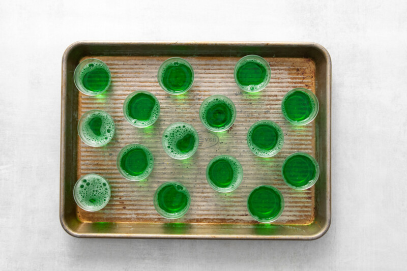 15 unset grinch jello shots on a rimmed baking sheet.