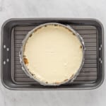 a cheesecake in a baking pan on a marble countertop.