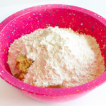 flour in a pink bowl on a white surface.
