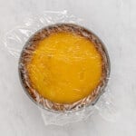 lemon cheesecake with a layer of plastic wrap on top