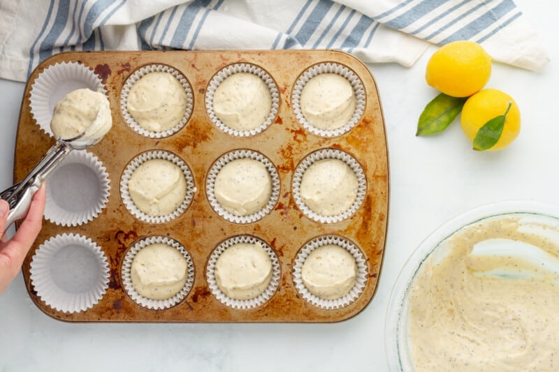 hand pouring scoops of muffin batter into a muffin tin