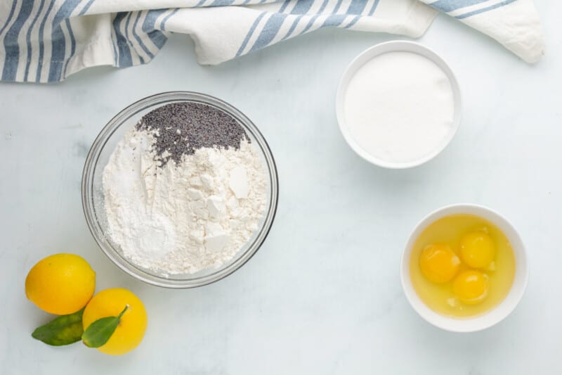 a bowl of flour, eggs and lemons on a marble table.