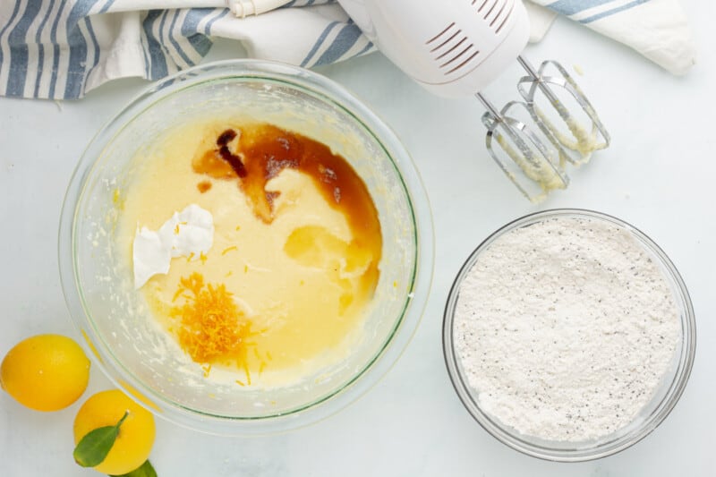 a bowl of flour, eggs and lemons next to a mixer.