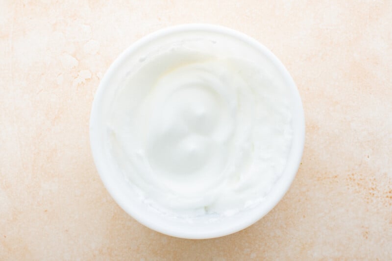 a white bowl of yogurt on a beige surface.