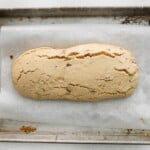 partially baked maple pecan biscotti loaf on a baking sheet.