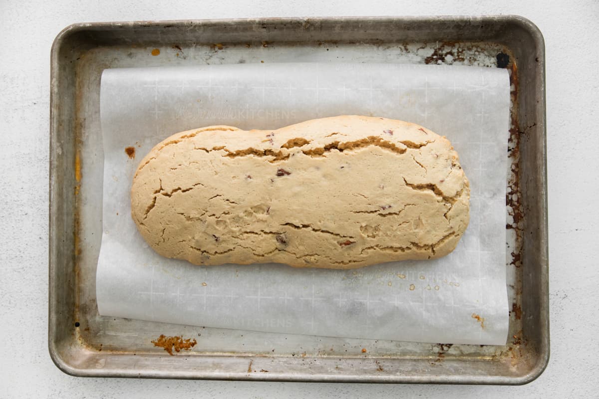 partially baked maple pecan biscotti loaf on a baking sheet.