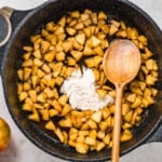 apples in a skillet with a wooden spoon.