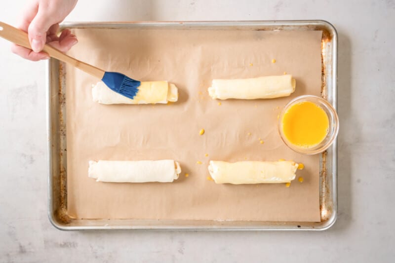 a person is using a brush to make rolls on a baking sheet.