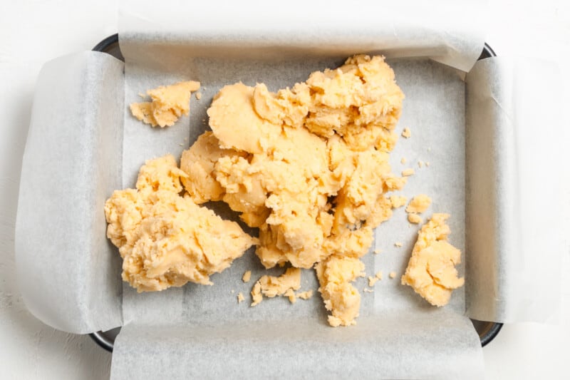 cookie dough piled into a baking pan lined with parchment paper