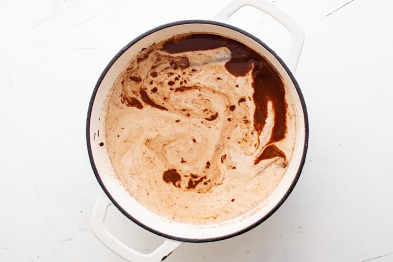 overhead view of chocolate and cream mixture added to cream in a white dutch oven.