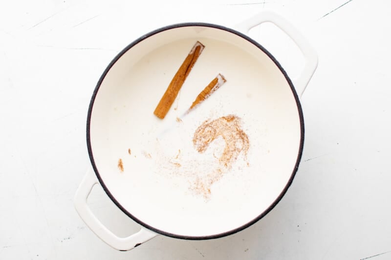 overhead view of milk, cream, sugar, and cinnamon sticks in a white dutch oven.