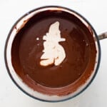 overhead view of hot cream added to melted chocolate in a glass bowl with a spoon.